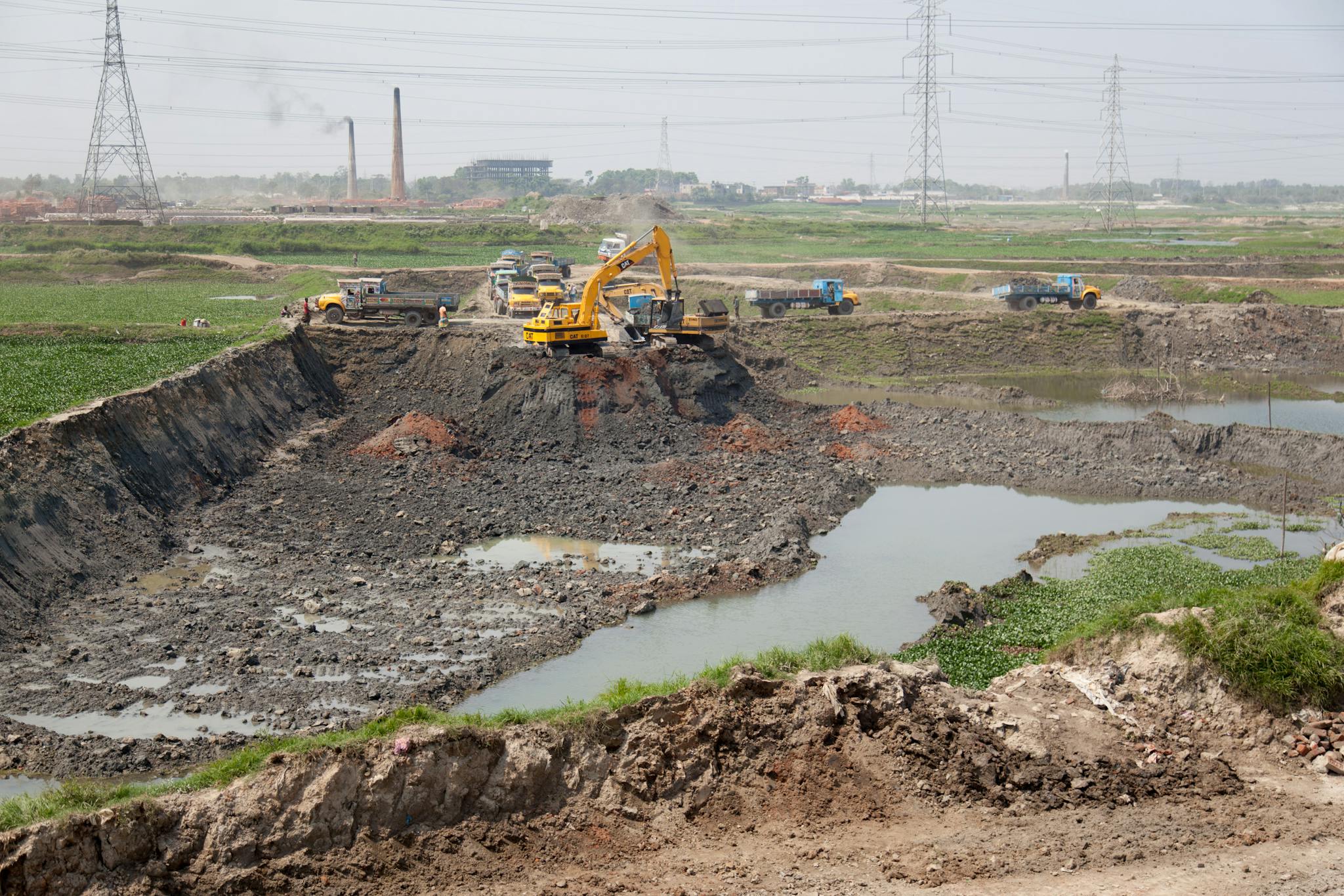 A wide view of a construction site with heavy machinery and trucks in Gabtoli, Dhaka, Bangladesh.