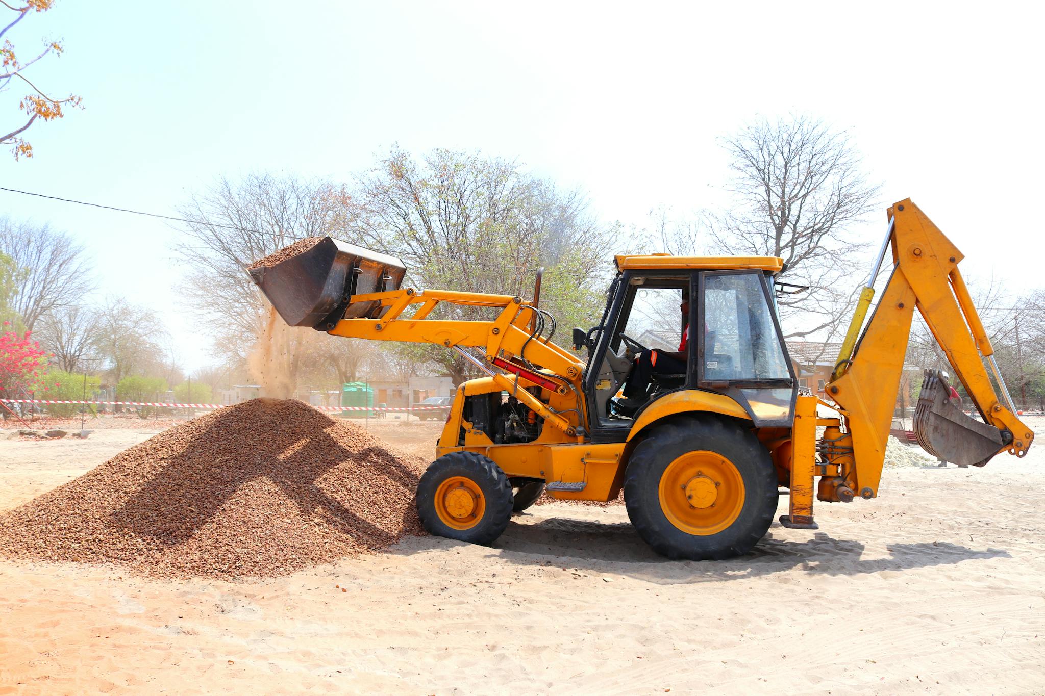 A yellow excavator moving gravel at an outdoor construction site during the day with clear skies.