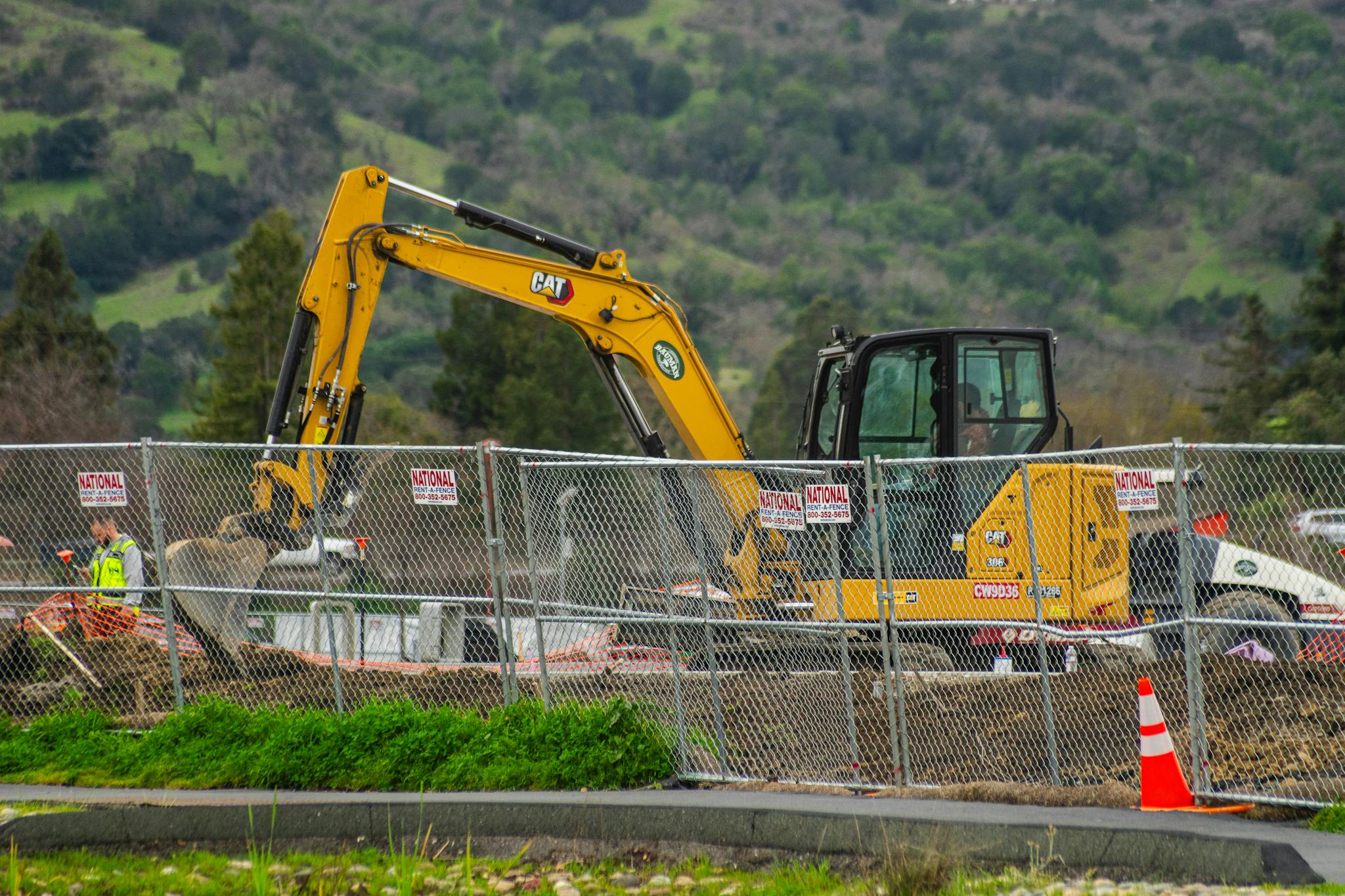Excavator working at a construction site with safety fences and workers, depicting industry work environment.