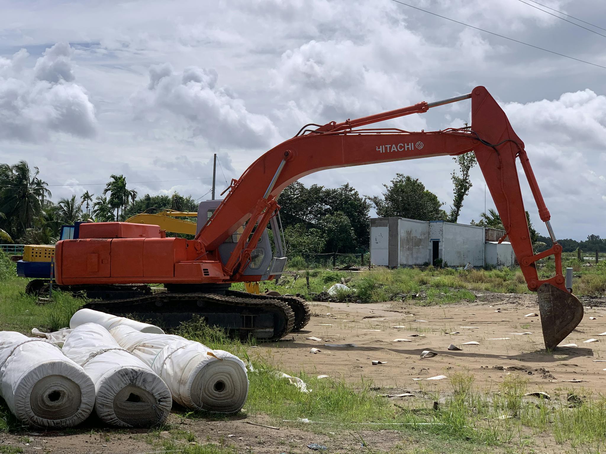 Orange excavator at a construction site on a sunny day with cloudy sky.